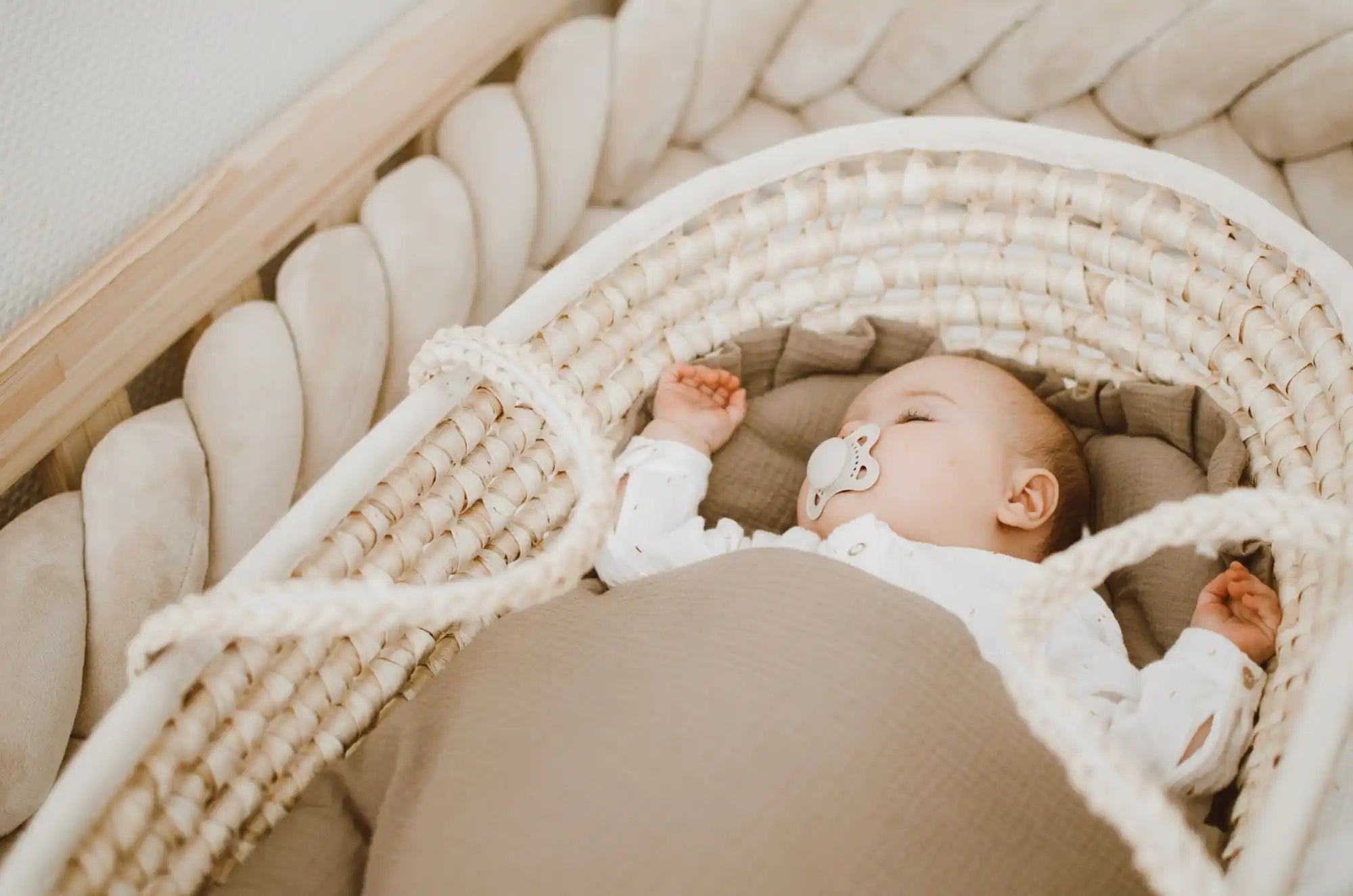Ein Baby, das in einem geflochtenen Moseskorb schläft, mit einem Schnuller.