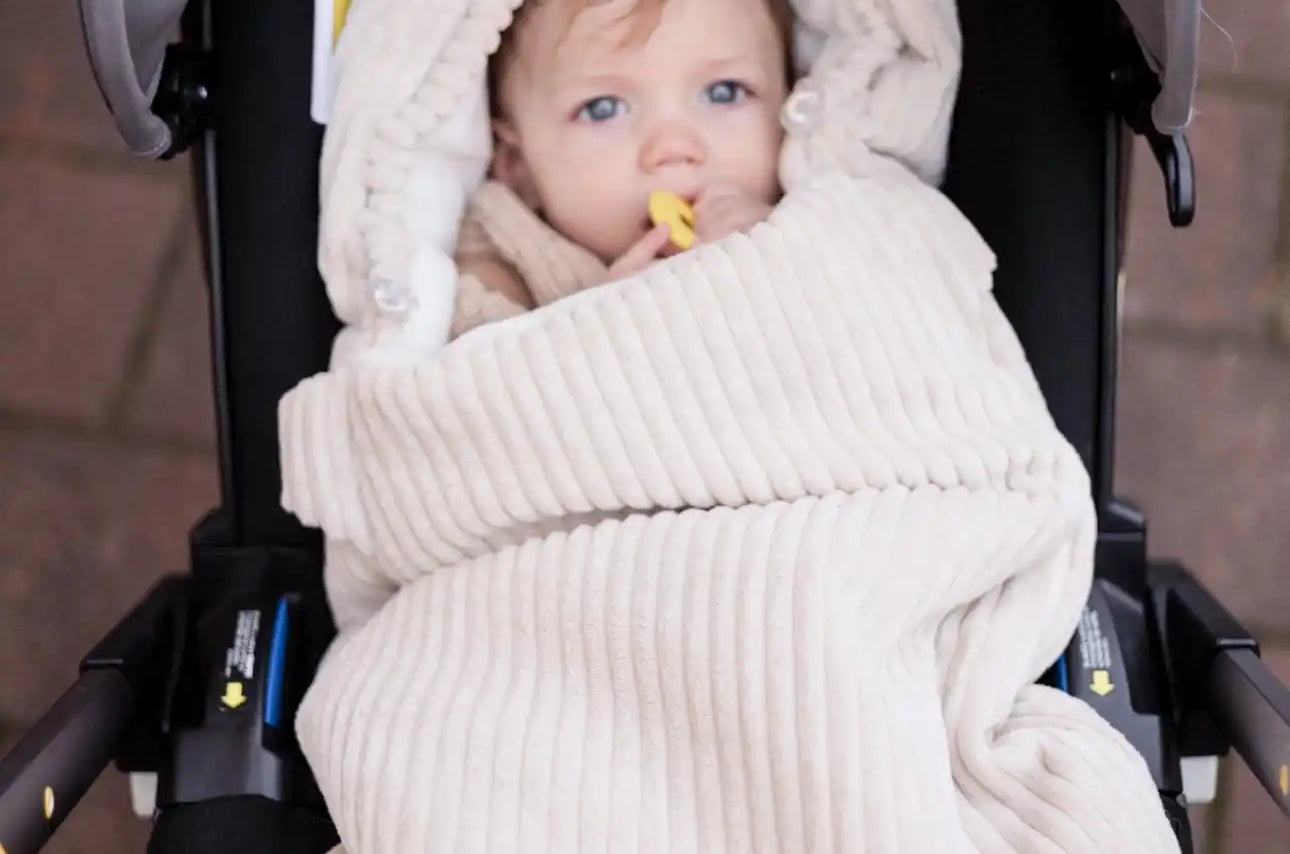 Ein Baby, das in eine cremefarbene Cordstoffdecke gewickelt ist, in einem Autositz.