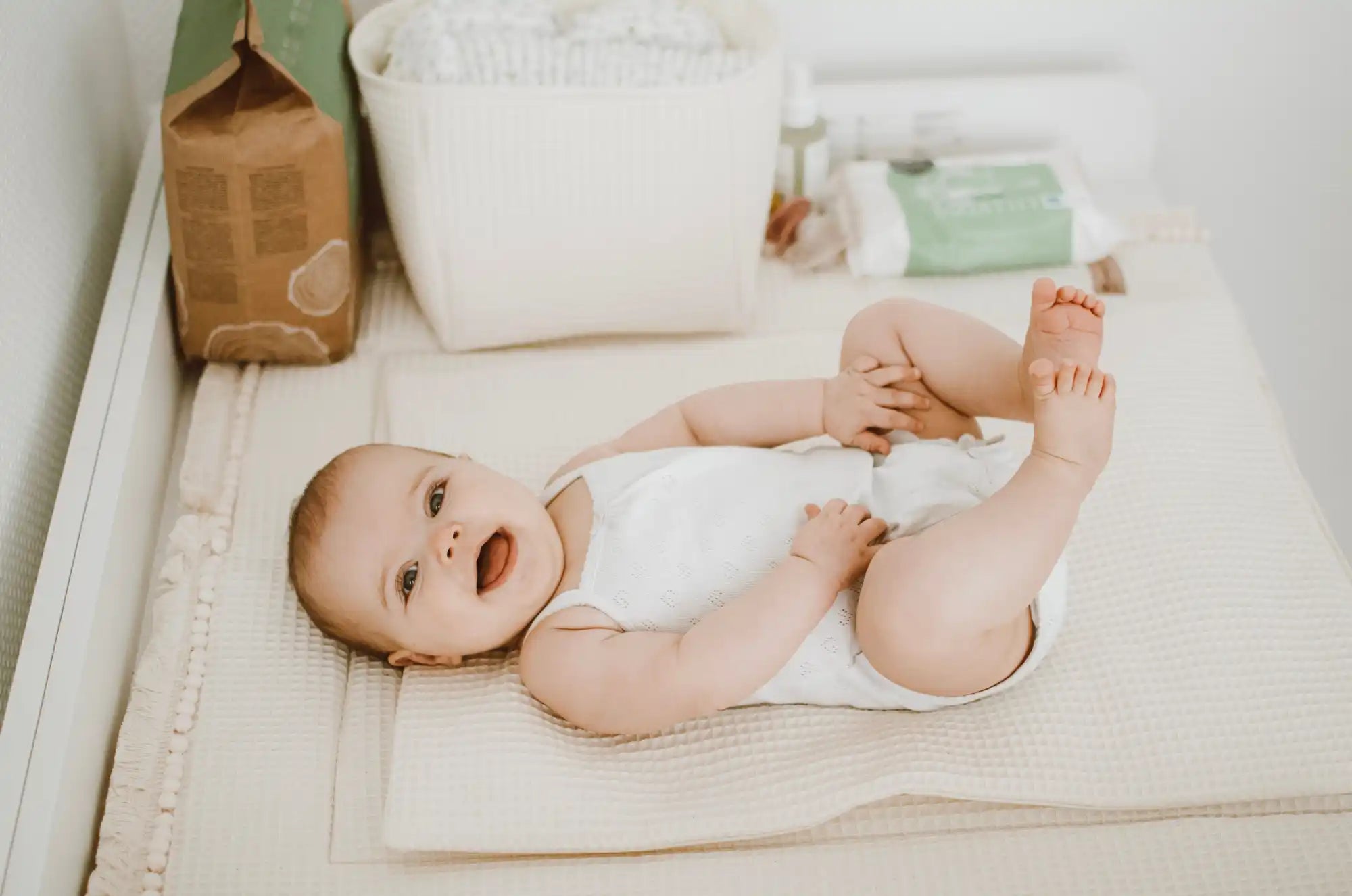 Ein Baby auf einer Wickelauflage, das einen weißen Body trägt.