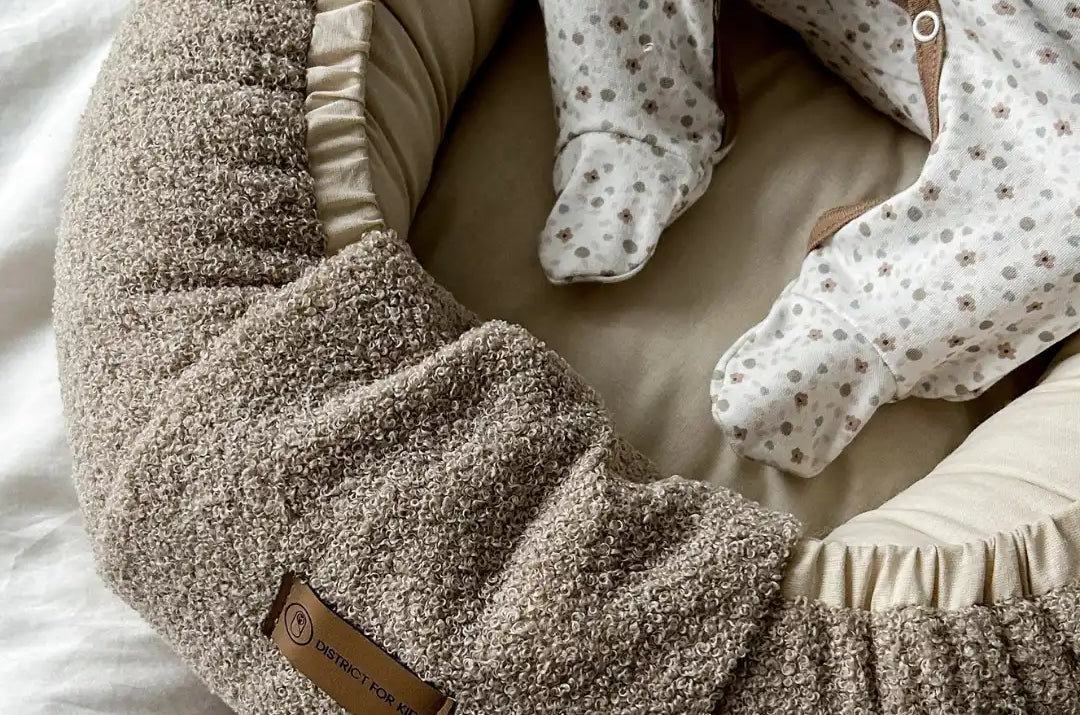 Ein gemütliches, strukturiertes, hellbraunes Babyschmuck mit einem cremefarbenen Inneren und einem Baby in einem Blumenpyjama.