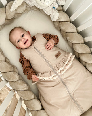 Baby lachend im Boho Kugelschlafsack im Babybett mit Bettschlange