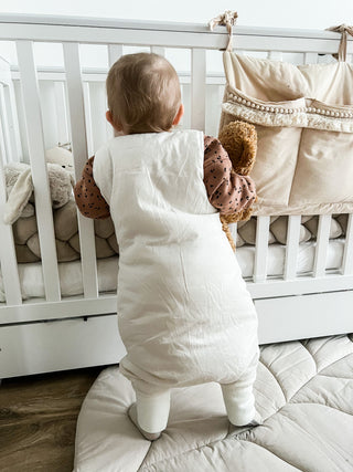 Baby am Babybett mit Schlafsack mit Füßen