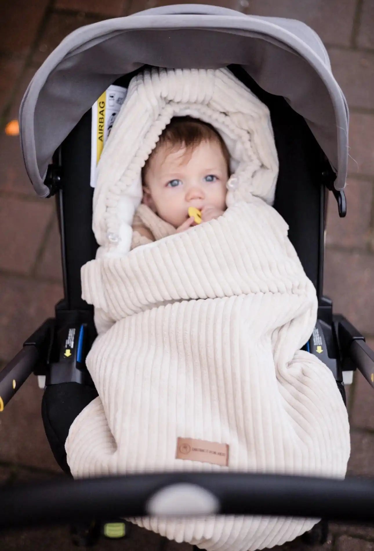Ein Baby, das in eine cremefarbene Cordstoffdecke gewickelt ist, in einem Autositz.