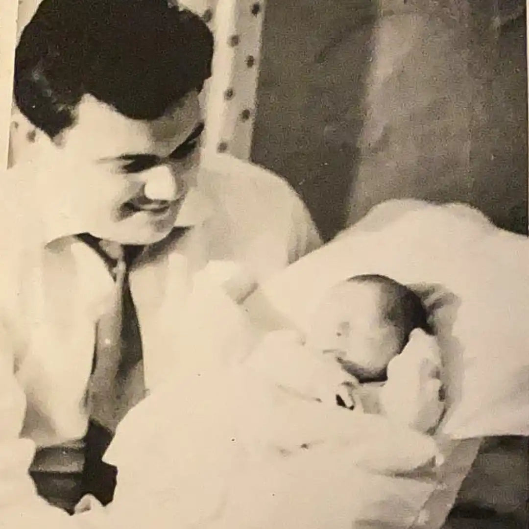 Ein Mann in einem Hemd mit Kragen und Krawatte, der ein neugeborenes Baby in eine Decke gewickelt hält.