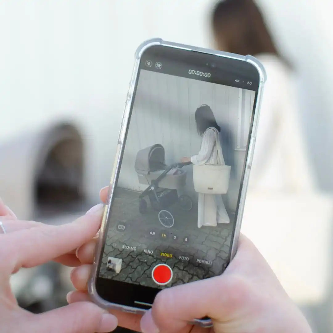 Ein Smartphone zeigt eine Videoaufnahme einer Frau mit einem Kinderwagen.