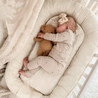 Baby schlafend in Kuschelnest mit Teddy in der Hand